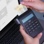 kenson Investments | How On-Chain Identity Changes Counterparty Review Person using a secure payment terminal beside a laptop.