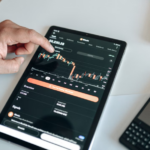 A black digital tablet displaying cryptocurrency price charts and market analytics.