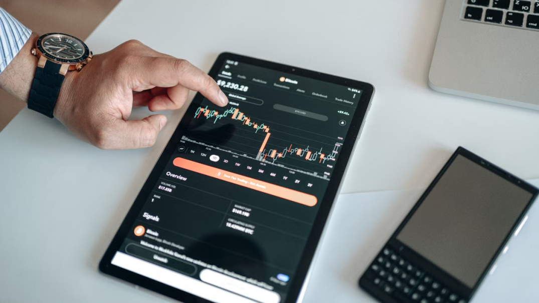 A black digital tablet displaying cryptocurrency price charts and market analytics.