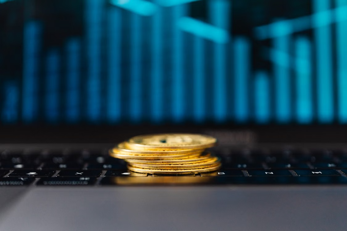 kenson Investments | Why Proof of Reserves Is Not Enough Stacks of gold cryptocurrency coins resting on an open laptop keyboard.
