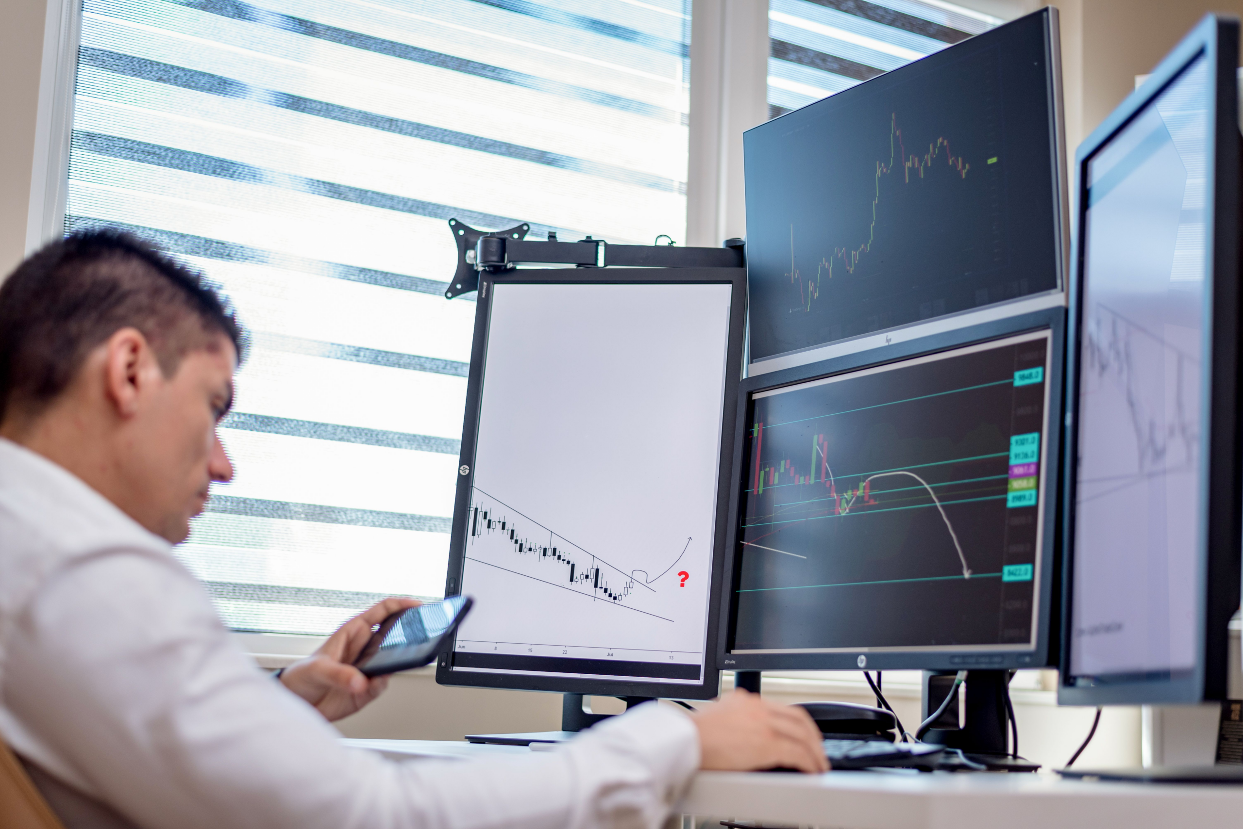 Financial analyst monitoring charts and transaction data across several computer screens