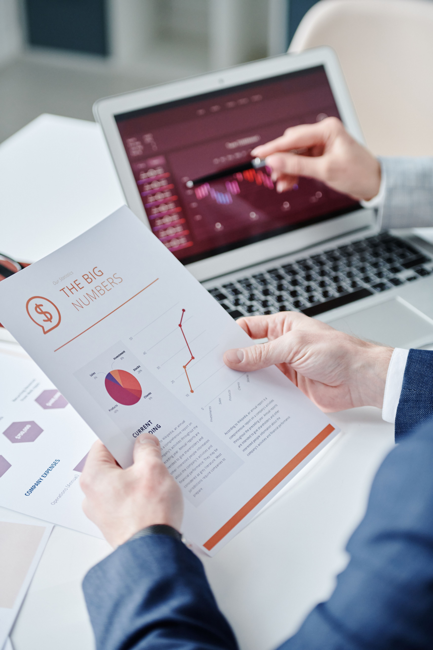 Professionals comparing financial charts on paper with data displayed on a laptopCaption: