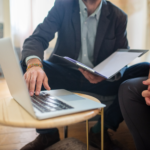 Professionals reviewing regulatory documents beside a laptop during an office consultation