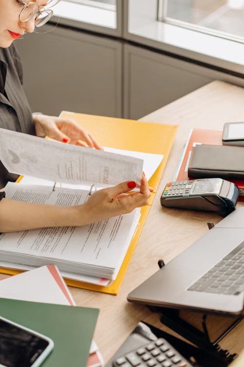 A person reviewing compliance documents and a laptop