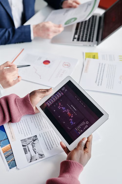 A close-up of hands reviewing printed charts and a tablet showing market trend data.