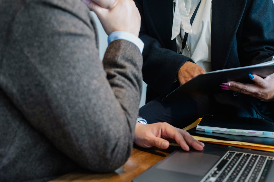 Two professionals reviewing compliance documentation on a laptop in an office setting.