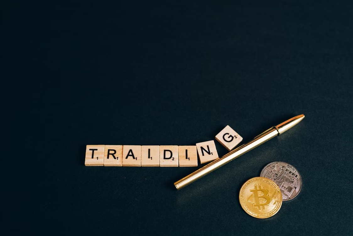 kenson Investments | Convergence of TradFi & DeFi via Programmable Settlement: Capital Markets Move to 24/7 Rails Pen resting next to coins.