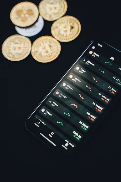 Smartphone showing financial charts surrounded by scattered coins on desk.