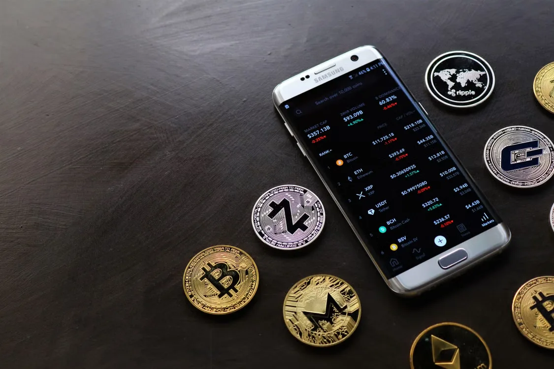 A collection of cryptocurrency coins and a smartphone displaying a digital trading platform
