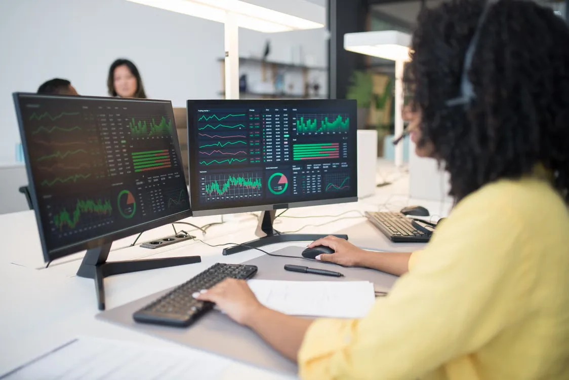 Analyst reviewing digital asset market data on multiple computer screens in a financial workspace.