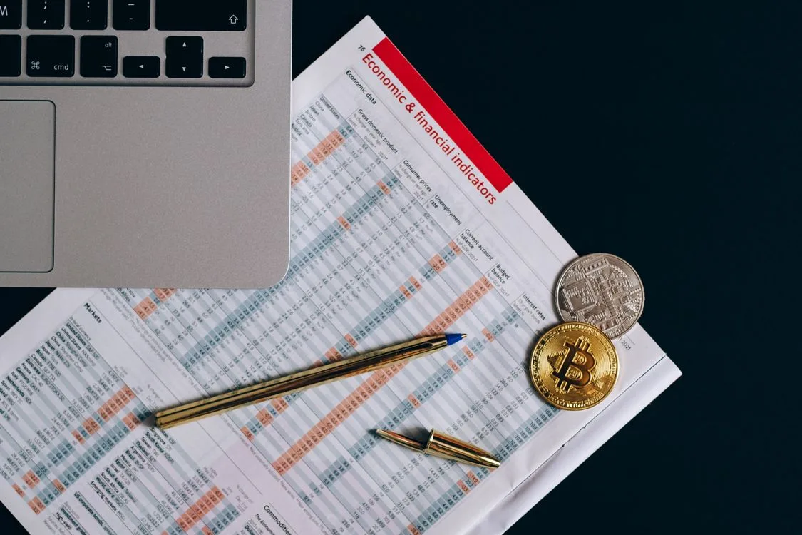 Top view of bitcoin coins on financial documents beside a laptop keyboard..