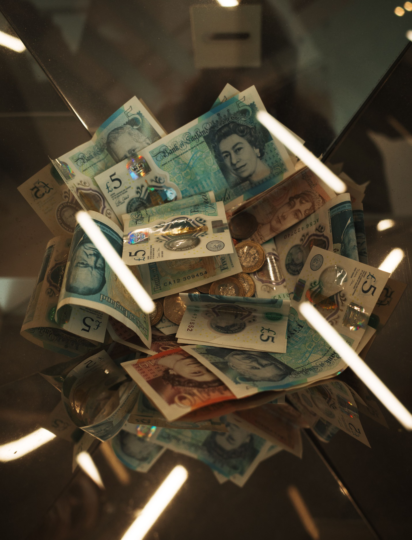 kenson Investments | The Bank of England Is Letting Stablecoins Settle Securities: What Has to Be True Before Wholesale Use Scales? British pound notes and coins inside a glass container representing stablecoin reserve backing and asset safeguarding