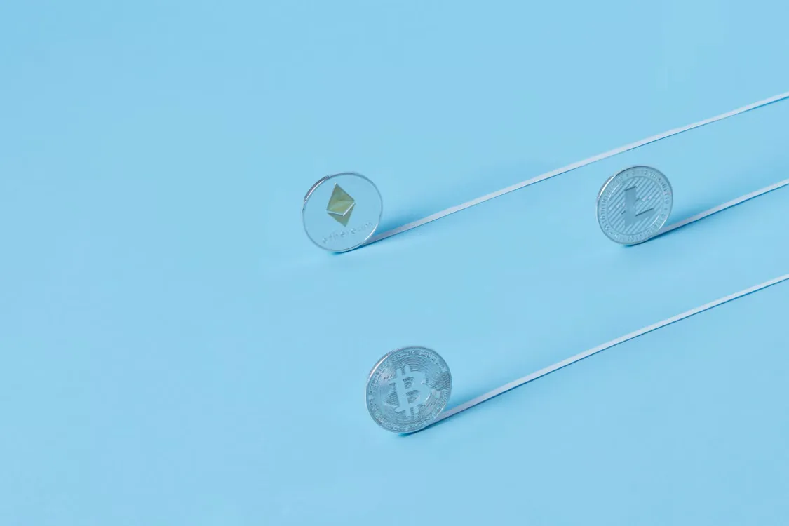 Minimalist image of Bitcoin, Ethereum, and Litecoin coins on a baby blue background.