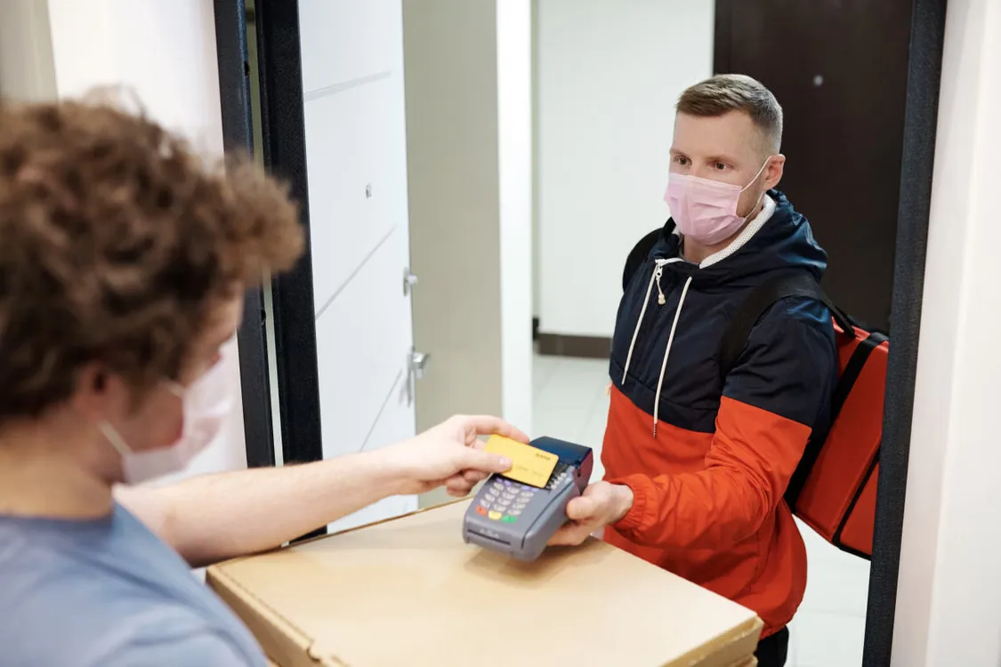 Masked deliveryman receiving payment for pizza delivery.