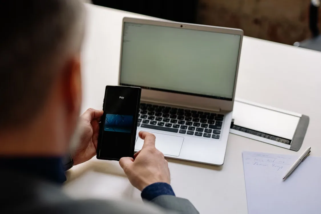 A person reviewing cryptocurrency wallet security settings on a phone beside a laptop.