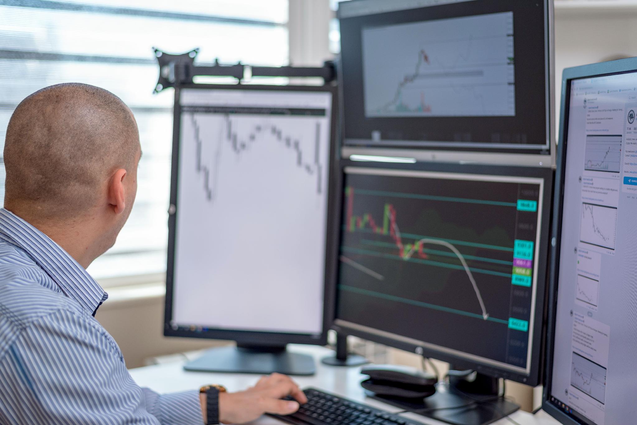 Multiple computer monitors displaying financial charts and market data at an electronic trading workstation