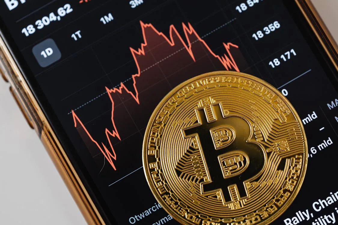 Bitcoin coin displayed over a smartphone market chart representing fees, compliance, and digital asset trading analysis.