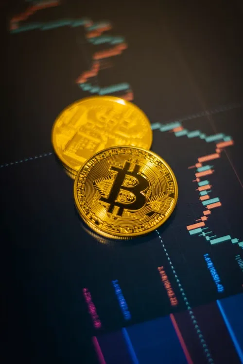 Bitcoin coins placed over a stock market chart showing price movements.