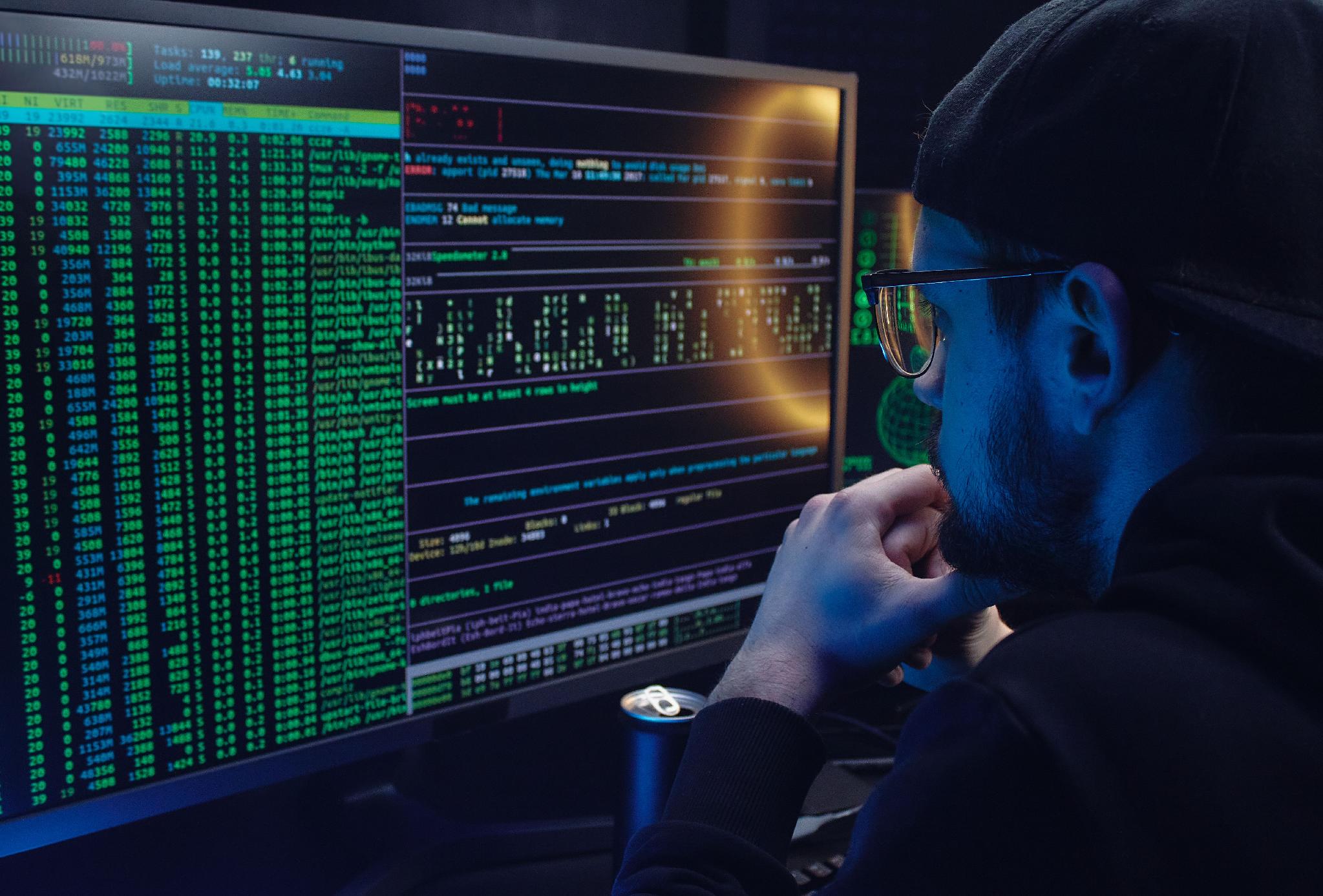 Software developer reviewing computer code across multiple monitors in a technical workspace