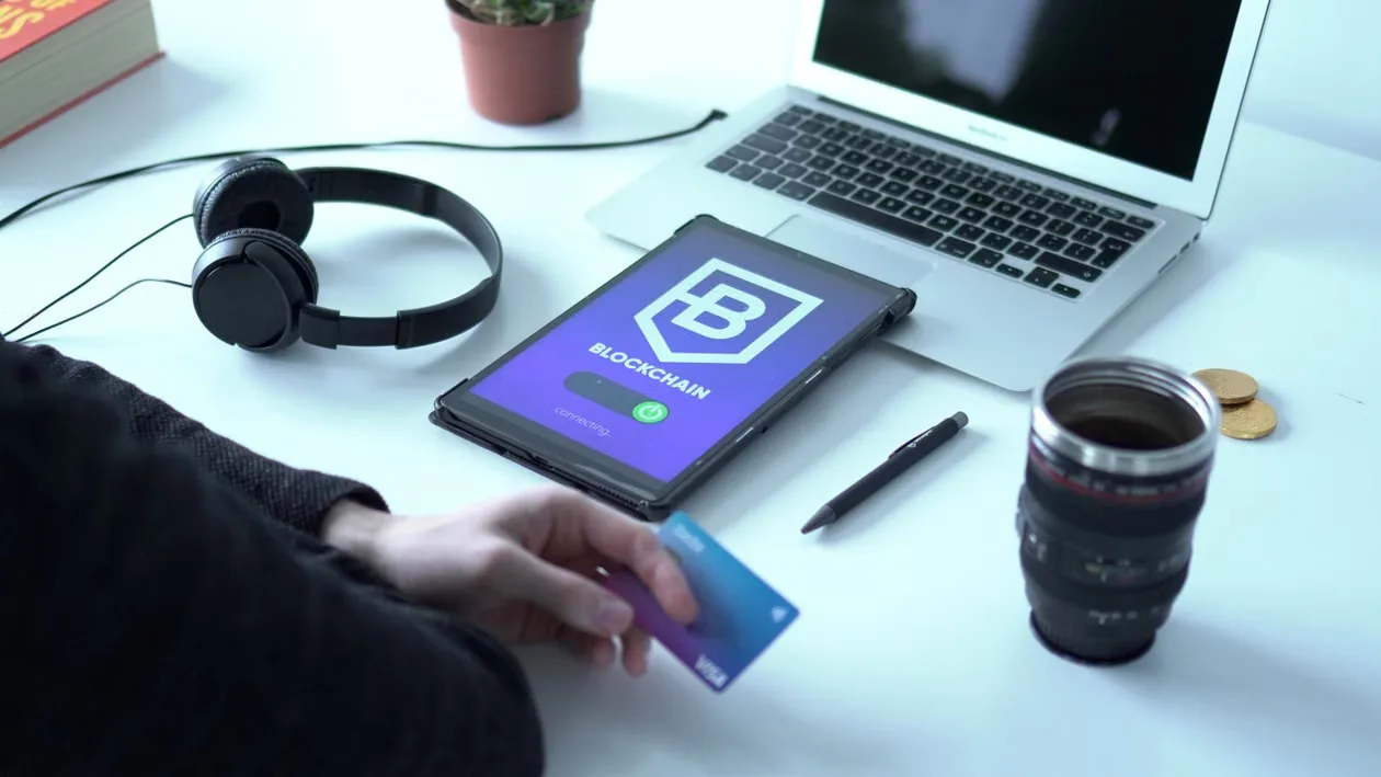 kenson Investments | Stablecoins Face a New Challenge: Turning Better Infrastructure Into Real-World Adoption Modern workspace featuring blockchain technology. Laptop, tablet, and card on a desk.