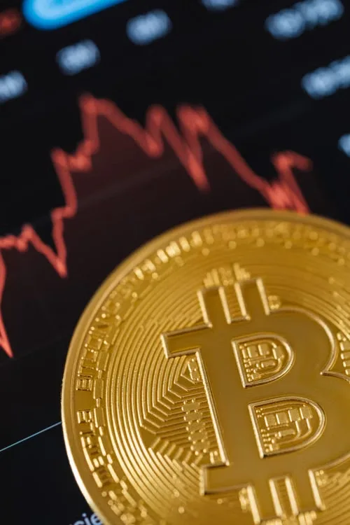 kenson Investments | Crypto Custody Explained: Questions to Ask About Who Controls Your Digital Assets Close-up of a gold Bitcoin coin with a fluctuating stock market graph in the background.