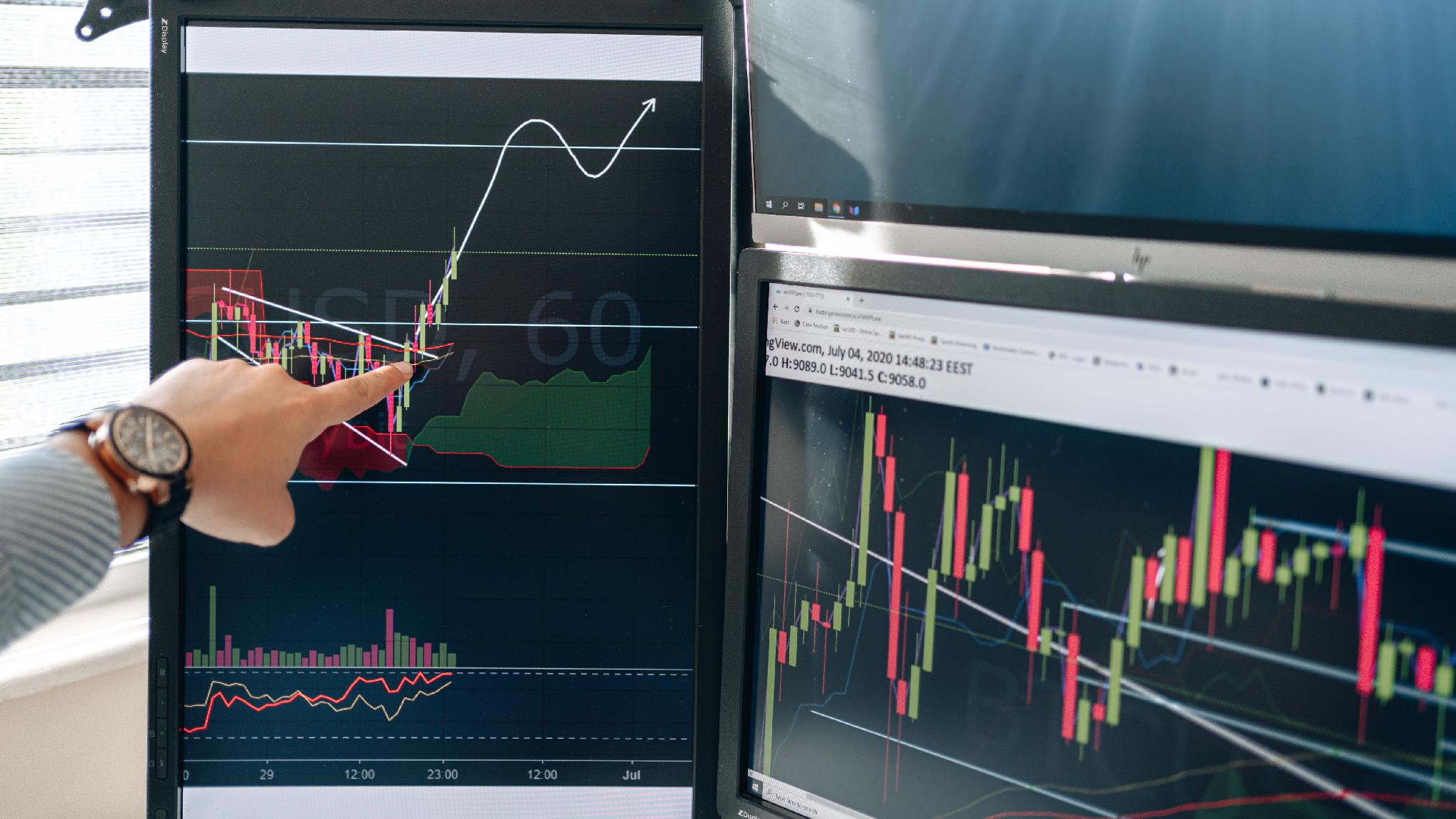 Finance professional reviewing market graphs on multiple trading monitors