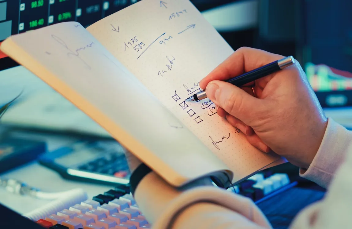 kenson Investments | Blockchain Account Permissions Explained: How Delegated Access Changes Digital Asset Security A hand writing in a notebook during analysis on a desk.