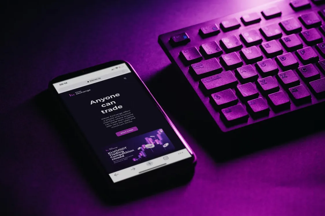 A photo showing a smartphone next to a keyboard under a purple light.