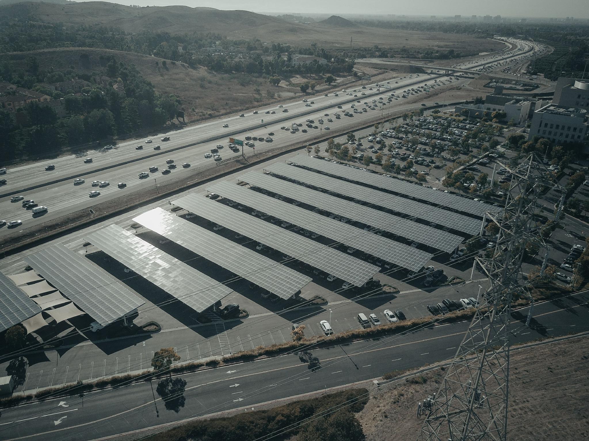 Aerial view of a solar energy facility beside a highway with power lines and moving traffic