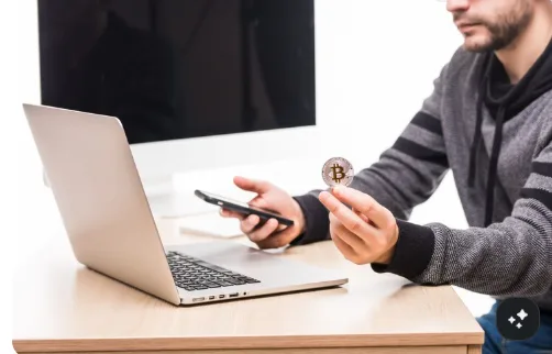 kenson Investments | Principles-Based Disclosure for Crypto Offerings: What Purchasers Would Actually Receive Person holding a smartphone while working with Bitcoin on a laptop.