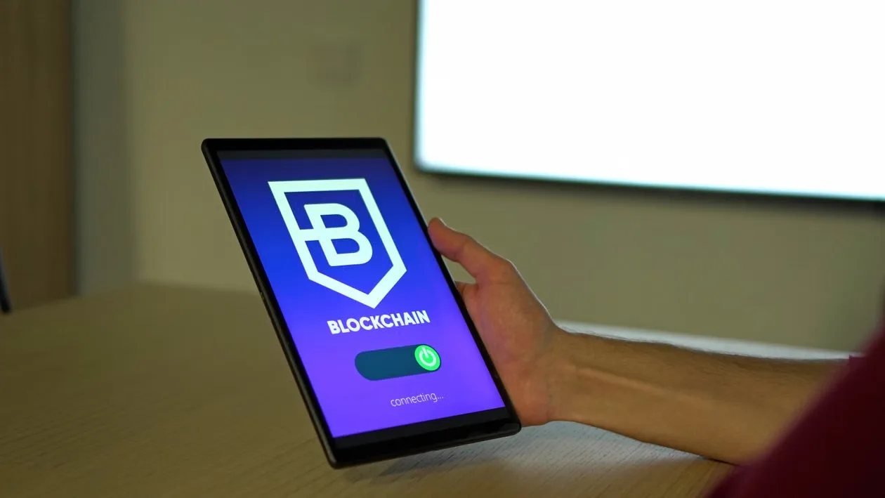 kenson Investments | Stablecoins Face a New Challenge: Turning Better Infrastructure Into Real-World Adoption A hand holding a tablet with a blockchain logo on screen