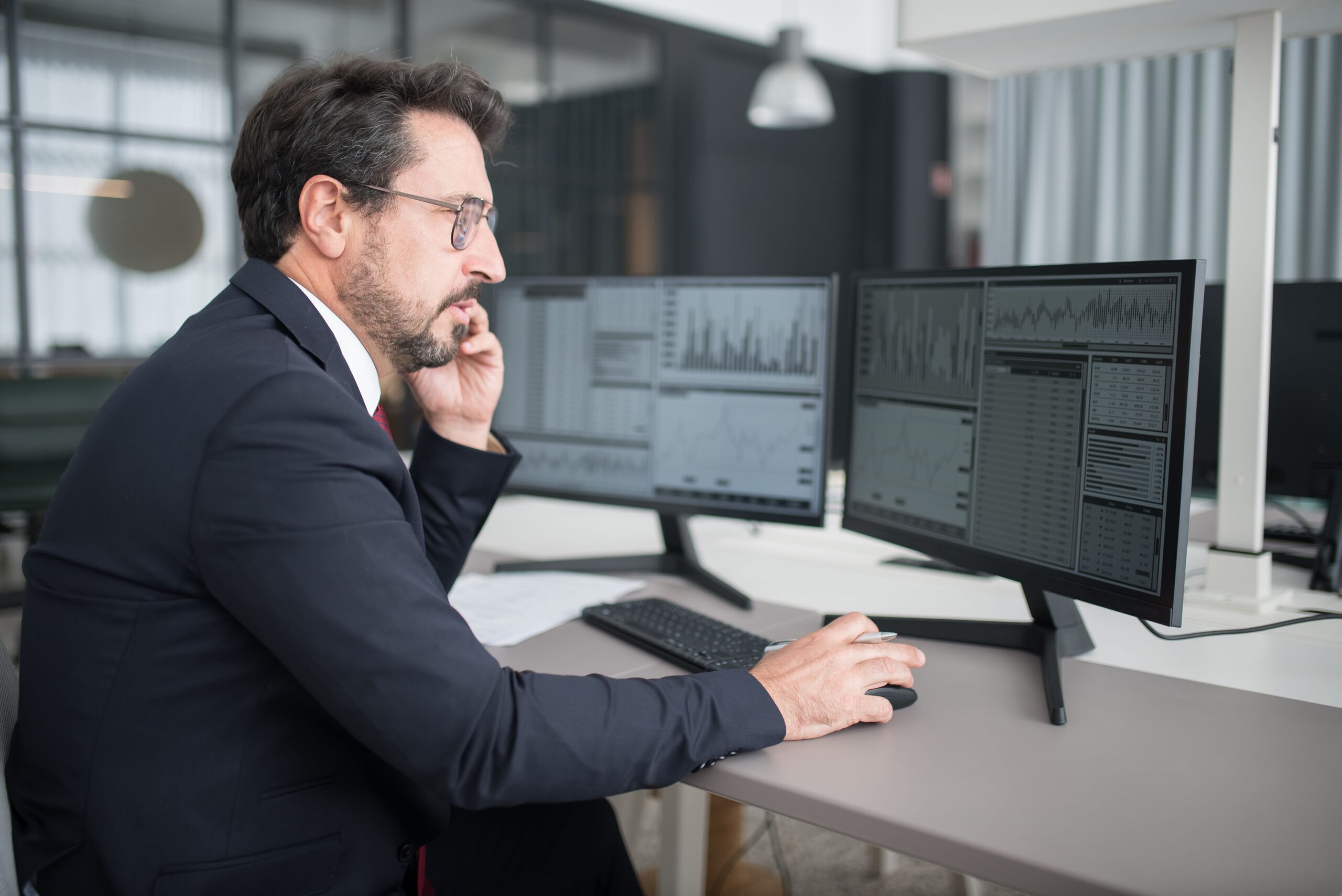 Investor monitoring financial market charts across multiple trading screens