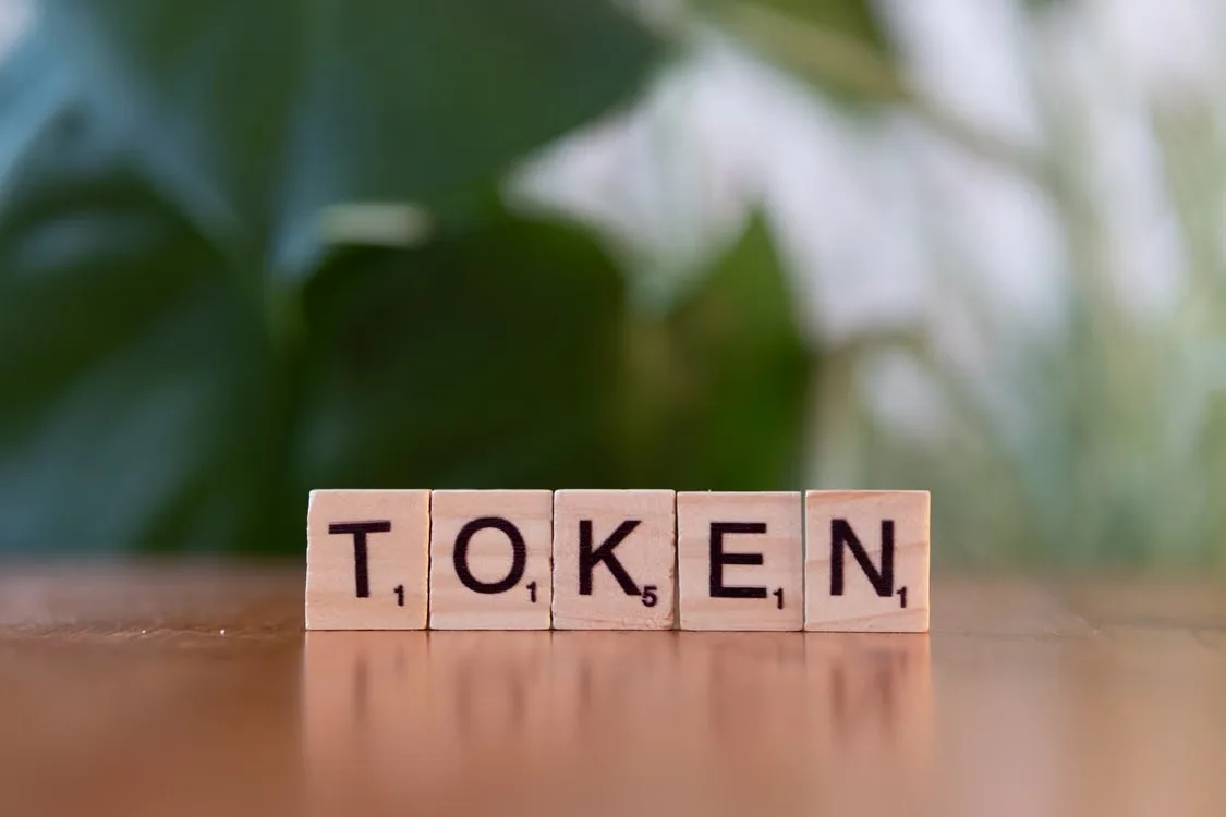 kenson Investments | Rebasing and Transfer-Fee Tokens: Reconciling Quantity Changes Scrabble tiles spelling “token” on a wooden surface.